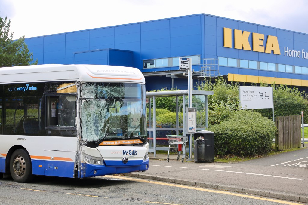 A damaged McGill's bus parked at a bus stop outside an IKEA store, with broken glass visible on the front.